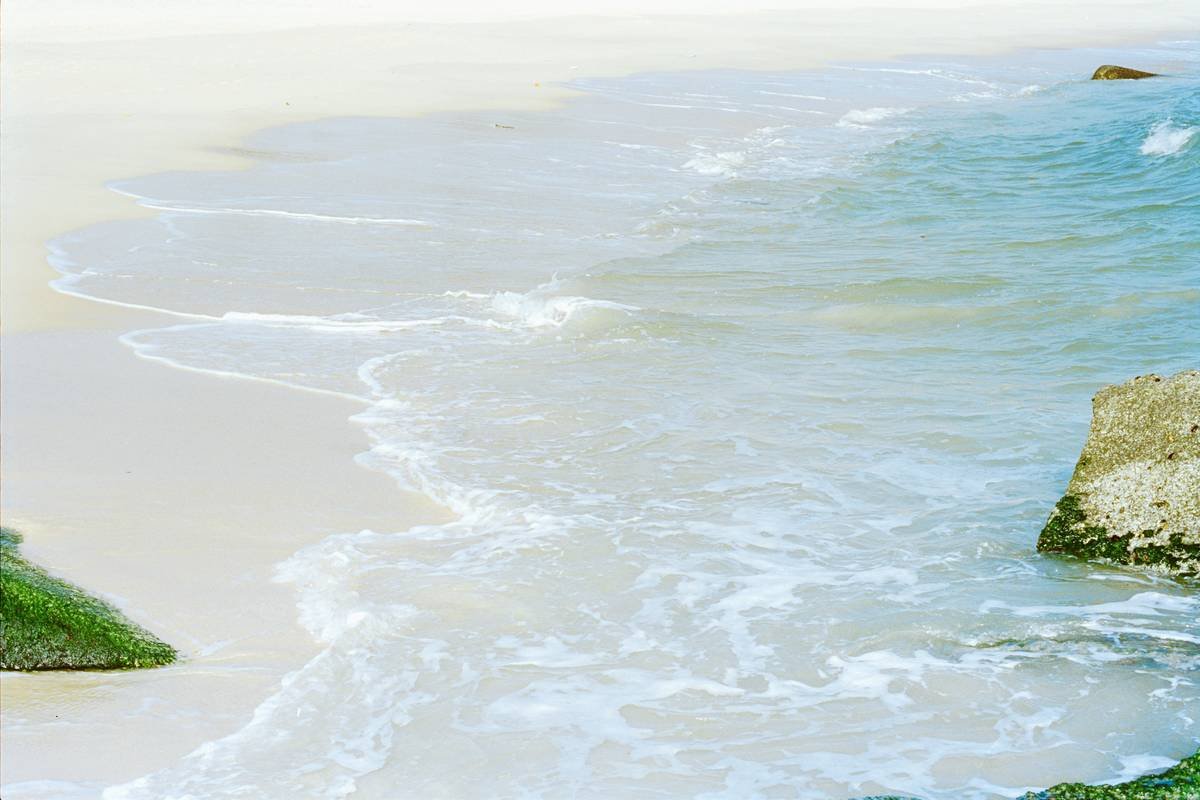 Gentle waves wash over a sandy beach with rocks.