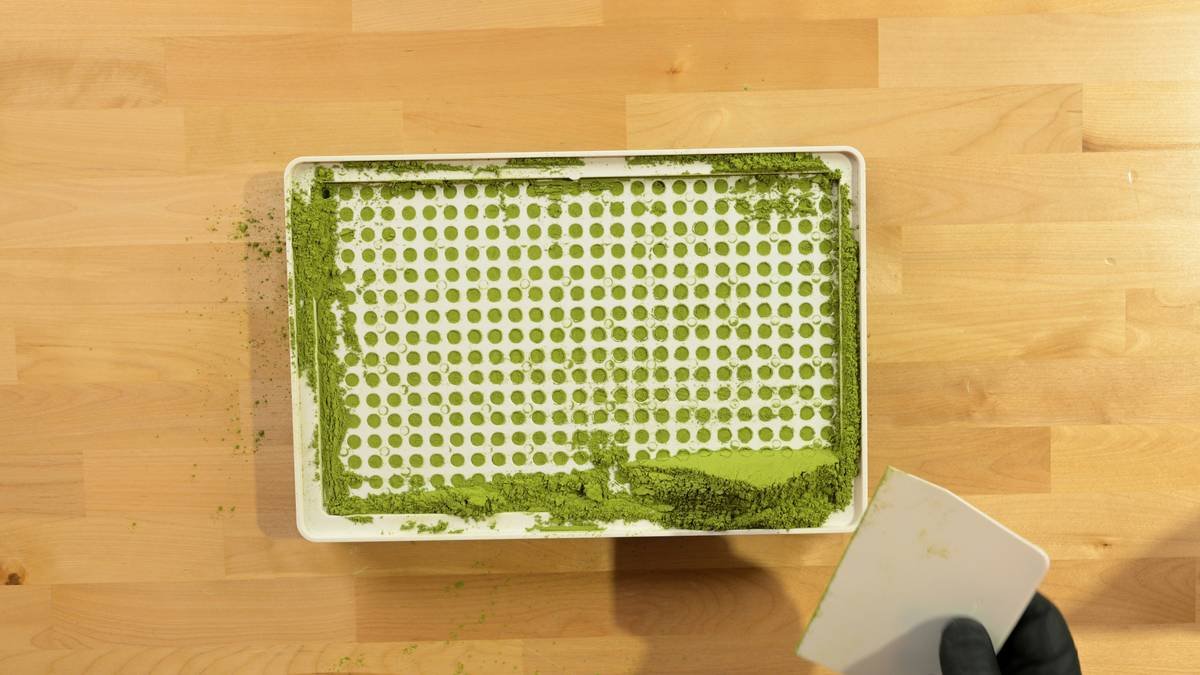 Spreading herbal green powder into empty capsules using a Cap & Press™ Core Series 400 Hole capsule filling machine from a top overhead view - Photo courtesy of https://blated.com - credit appreciated